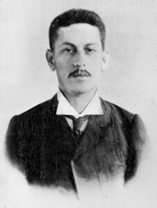Formal photo portrait of a man, perhaps in his 30s, wearing a suit and tie of the sort fashionable around 1900.