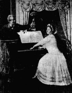 A woman plays the piano as a man holds a lamp over the sheet music.